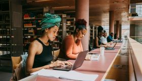 Woman wearing turban using laptop while sitting with friend in library