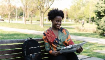 Portrait of a young woman sitting at the park and reading newspaper