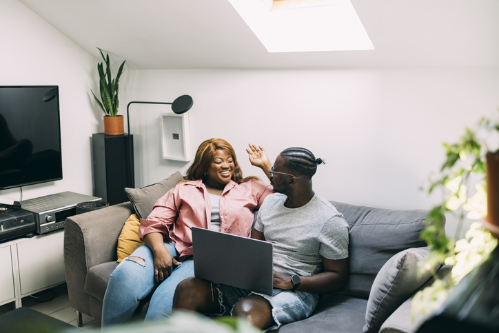A Happy Couple Working Together From Home Using Their Computer While Sitting On The Sofa