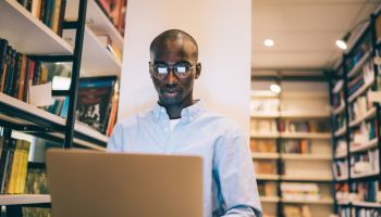 Black man in glasses using laptop in library