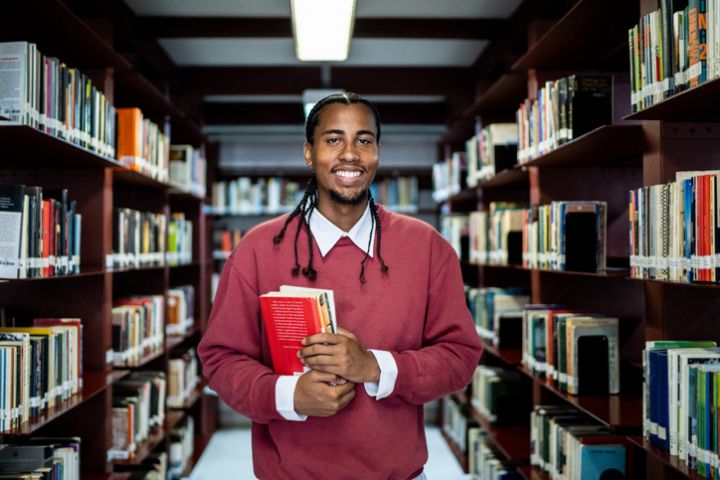 Portrait of a young man holding a book in a library
