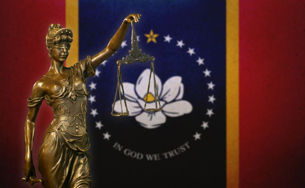 Close-up of a small bronze statuette of Lady Justice before a flag of Mississippi (USA).