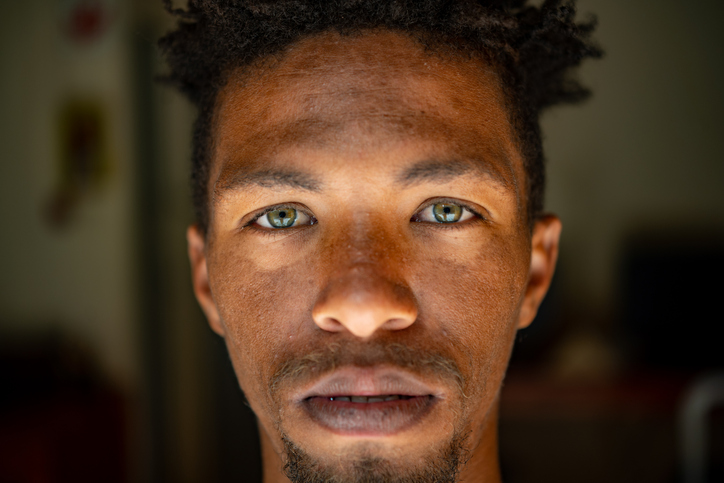 Extreme Close up Serious Headshot Landscape Portrait of young mixed race male face with green eyes facial hair and rasta hair