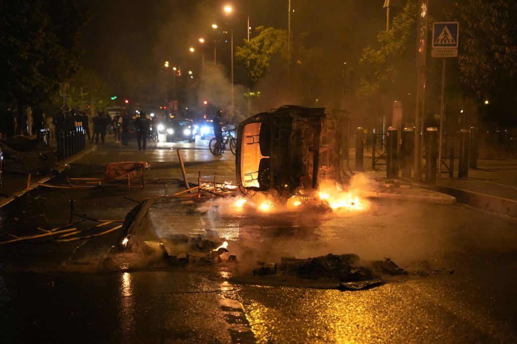 Riot police stand near a burning vehicle