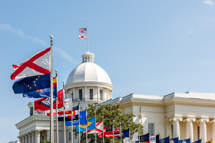 Montgomery, USA State capitol building in Alabama during sunny day with old historic architecture of government and many row of flags by dome