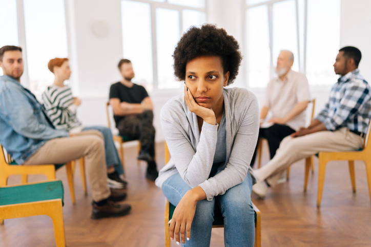 Portrait of unhappy African young pensive woman looking away during group therapy session, multicultural and different ages people sitting in circle