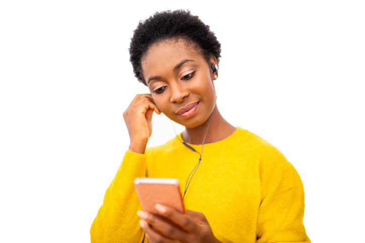 young black woman holding mobile phone and listening to music with earphones against isolated white background