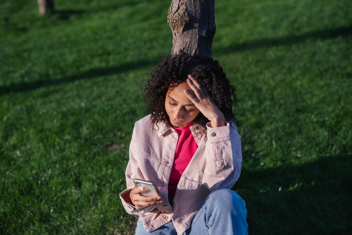 High angle view of teenage girl sitting in a park and scrolling her smartphone.