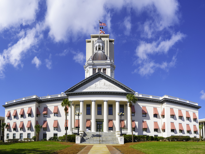 Historic Florida State Capitol Building with brightly colored striped awnings, classical style dome, and American and Florida State Flags in Tallahassee