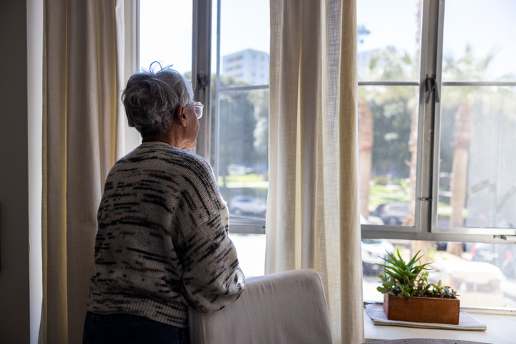 Senior woman looking out the windows of her home