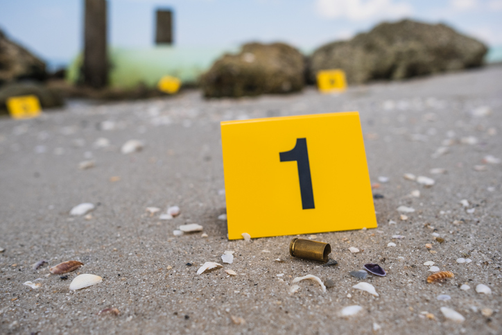 One yellow crime scene evidence marker on the beach after a gun shooting brass bullet shell casing 9mm handgun pistol