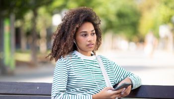 young african american woman sitting on park bench with mobile phone