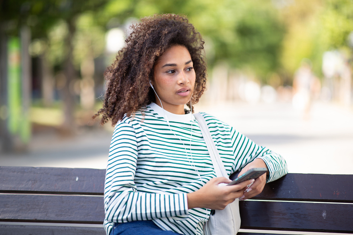 young african american woman sitting on park bench with mobile phone