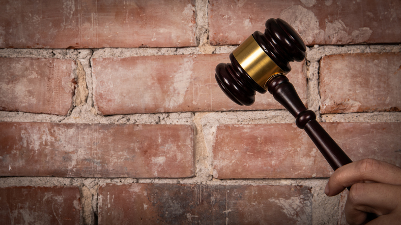 Judge hand holding gavel. Red brick background