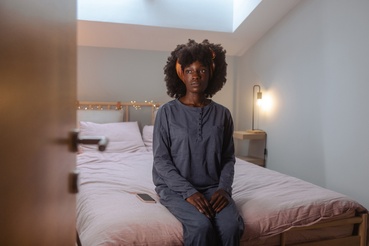 Depressed African American young woman sitting on the bed