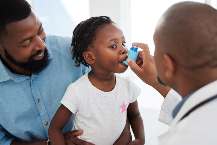 Doctor helping a child patient with an asthma inhaler in his office at the medical clinic. Healthcare worker consulting a girl with chest or respiratory problems with pump in a children's hospital