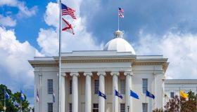 Montgomery Alabama State Capitol building with columns, steps, Dome, flag and Clock showing