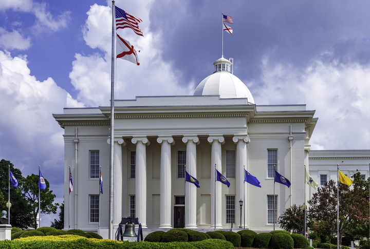 Montgomery Alabama State Capitol building with columns, steps, Dome, flag and Clock showing