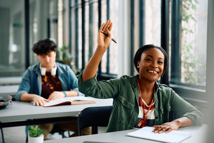 Happy black student raising her hand to answer the question during a lecture in the classroom.