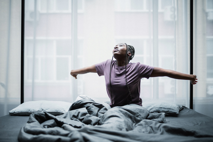 Good morning. Young black woman wakes up in a cozy bedroom. Feeling good and balanced after slept well