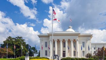 Montgomery Alabama State Capitol building with columns, steps, Dome, flags, a Liberty Bell replica, and beautiful landscaping