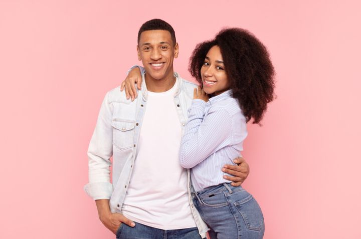 Portrait of black romantic couple embracing while posing over pink studio background, young man and woman hugging and smiling at camera