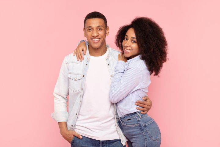 Portrait of black romantic couple embracing while posing over pink studio background, young man and woman hugging and smiling at camera