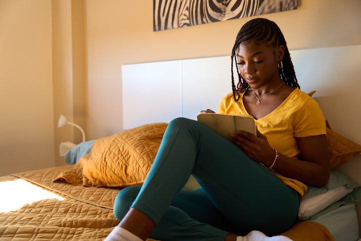 Young woman relaxing on bed while writing in notebook