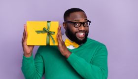 Portrait of positive nice man hold giftbox beaming smile look camera isolated on purple color background