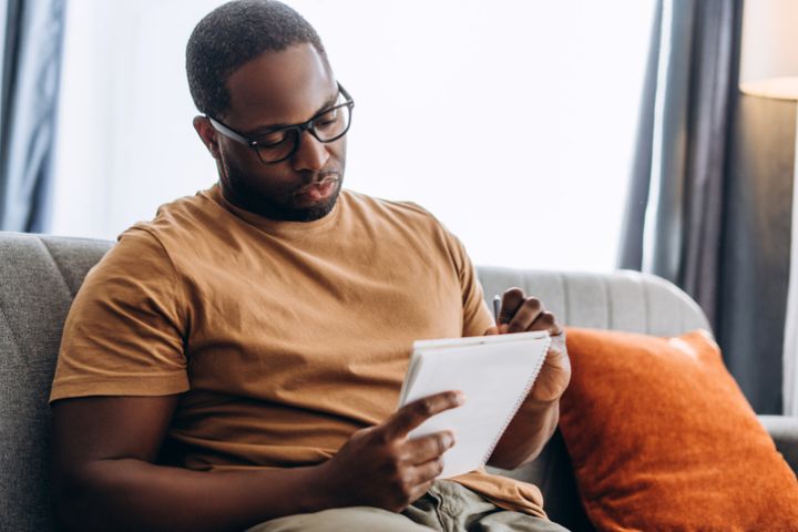 Calm African American man making notes sitting on sofa at home