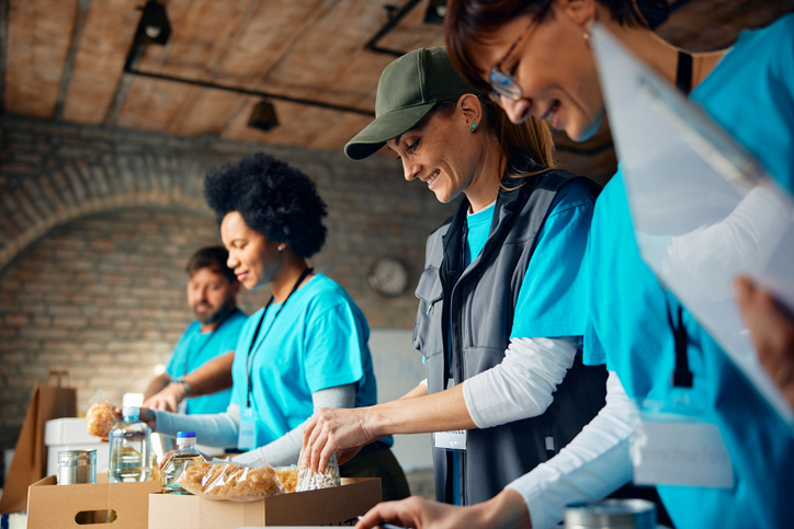 Happy woman packing donated food with group of volunteers at community service center.