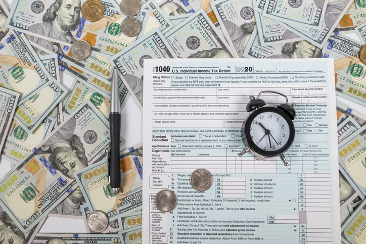 Tax form 1040 with a pen and an alarm clock on a dollar background. View from above. Tax time.