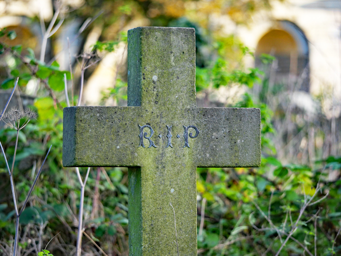 RIP (Rest In Peace) on the weathered stone cross of an ancient tomb at Brompton Cemetery. London, England, United Kingdom. Sunlight. Colors.