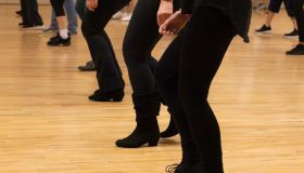 Lower legs of a small group of people doing line dancing indoors on a wooden floor while wearing black pants and boots. Line Dancing