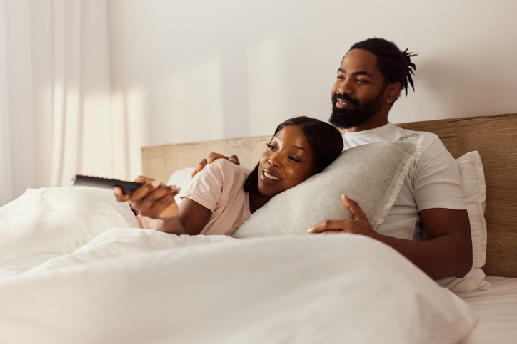 Happy African American couple watching TV in a bed.