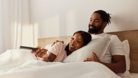 Happy African American couple watching TV in a bed.