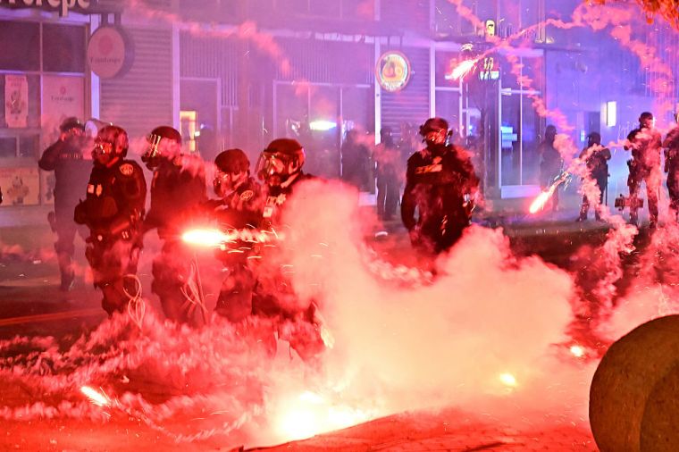 Fireworks burst around police officers clad in riot gear during protests