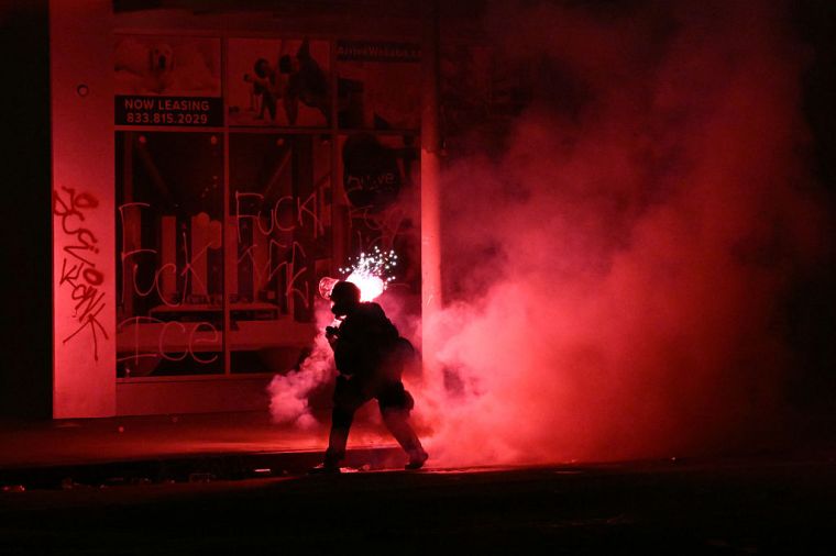 A firework explodes behind a police officer in riot gear during protests