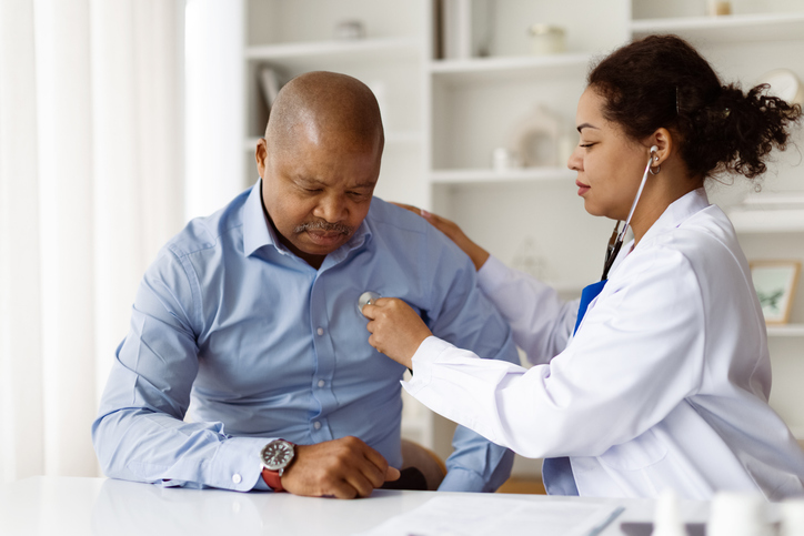 Mature black male patient undergoing chest examination with stethoscope during clinic checkup