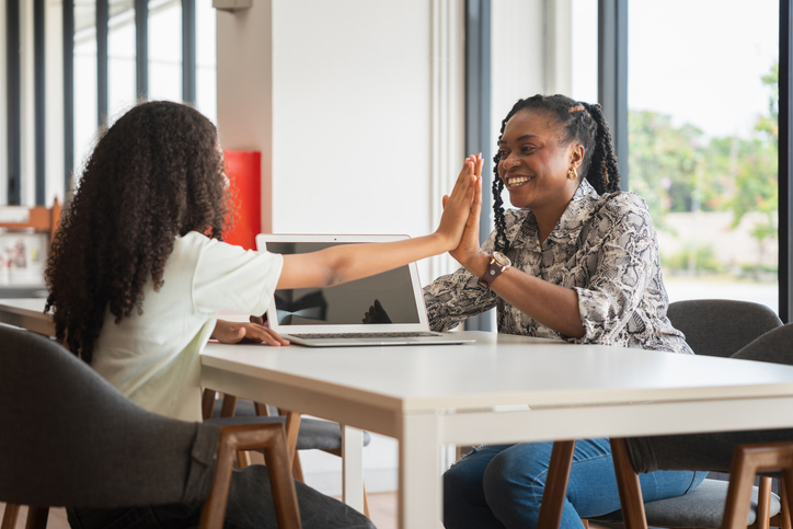 Joyful Female Tutor and Student High-Fiving in Modern Office, Teacher and Student Collaborating on Computer at Home, Mother and Daughter Studying Together with Laptop