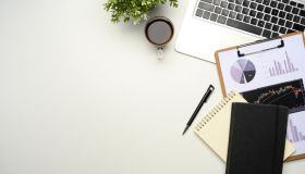 Flat lay of office desk with laptop, financial charts, notebooks, and coffee on white background
