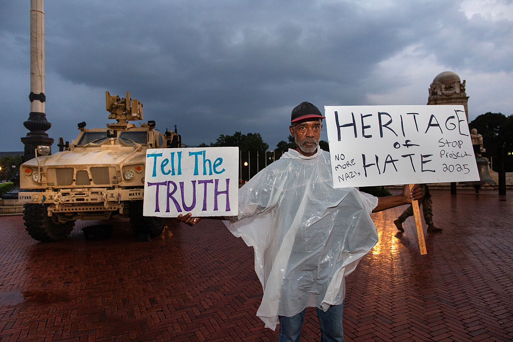 A man holding an anti-Trump sign stands in front of National...