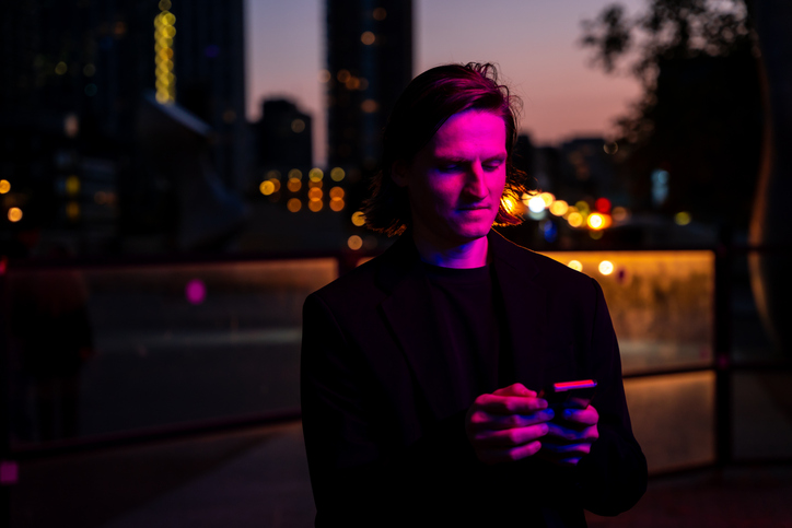 A young adult man using his smartphone outside at night