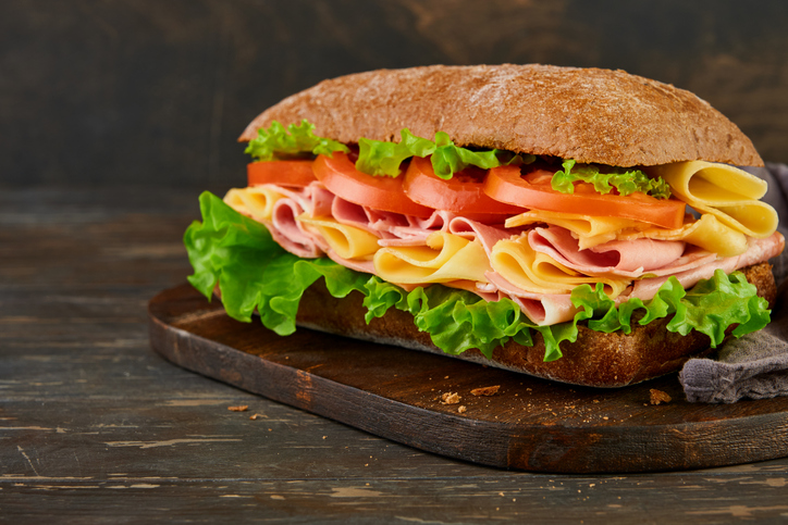 Sandwich. One fresh big submarine sandwich with ham, cheese, lettuce, tomatoes and microgreens on old wooden dark background. Healthy breakfast theme concept, school lunch, breakfast or snack.
