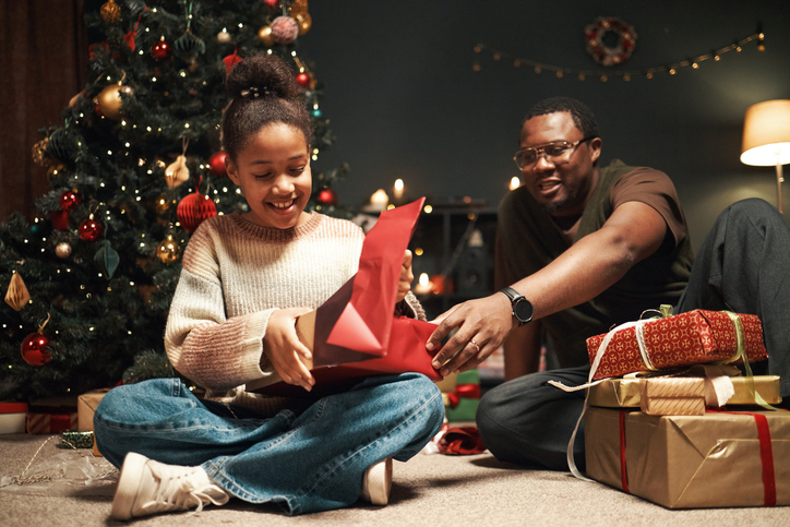 Smiling Black Girl Opening Christmas Gift with Middle Aged Black Man Watching