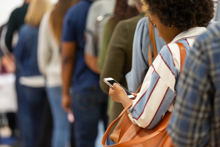 A diverse group of people patiently waiting in a line, focused on their mobile phones