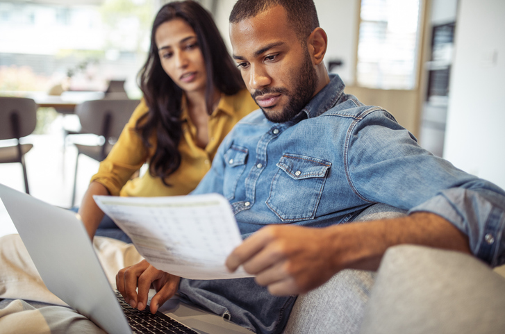 Engaged Couple Reviewing Financial Documents on Sofa Together