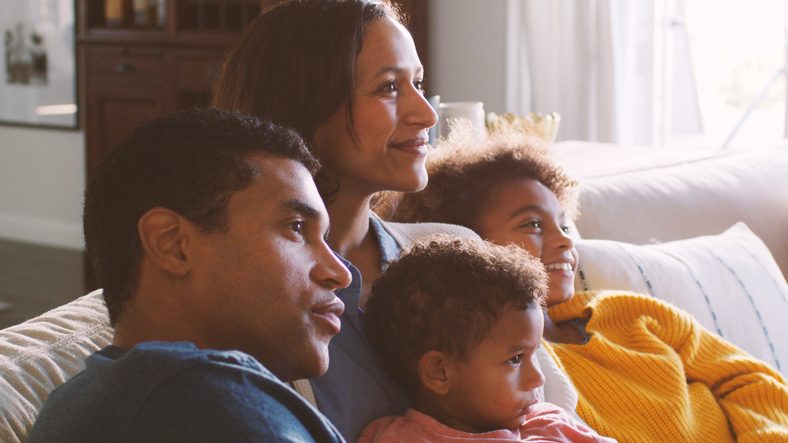Family At Home Sitting On Sofa Watching TV Together