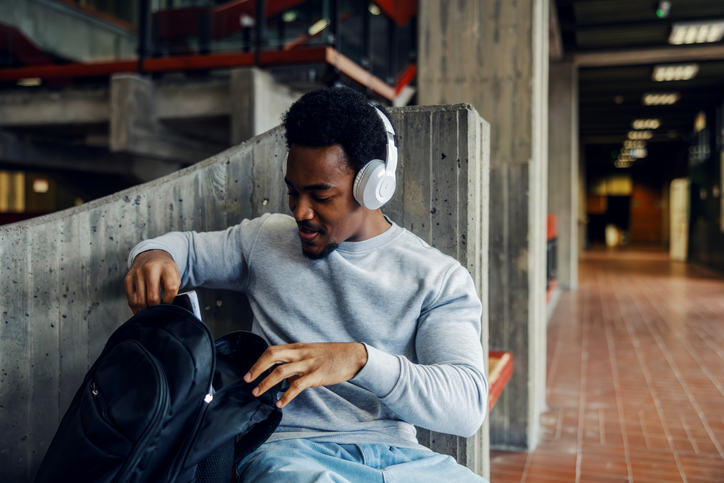 Black male student listening music wearing headphones at university