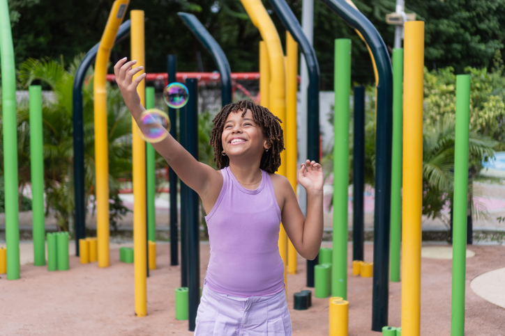 Happy african american child playing with soap bubbles in park